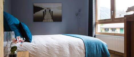 Een slaapkamer met een bed, nachtkastje, raam en een schilderij aan de muur.