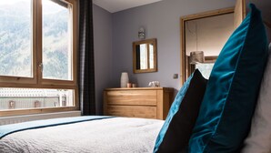 Una camera da letto con un letto, una cassettiera, uno specchio e una finestra vista montagne.