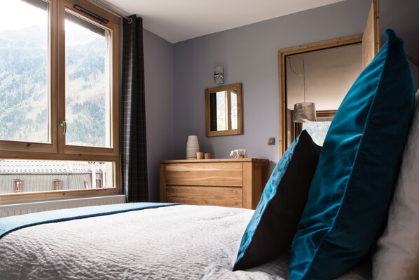 A bedroom with a bed, a dresser, a mirror, and a window with a view of mountains. - Le Beausite C Apartment -  an apartment that sleeps 5 guests  in 2 bedrooms (Chamonix-Mont-Blanc)