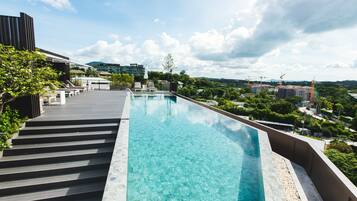 Una piscina infinita en la azotea con agua cristalina azul, rodeada por una terraza de madera y follaje.
