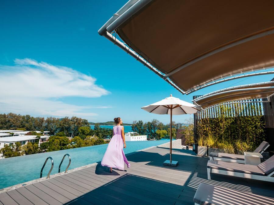 A poolside area with a woman in a long dress, lounge chairs, and a canopy.