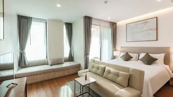 A modern hotel room with a large bed, a sofa, a small table, and a window with curtains.