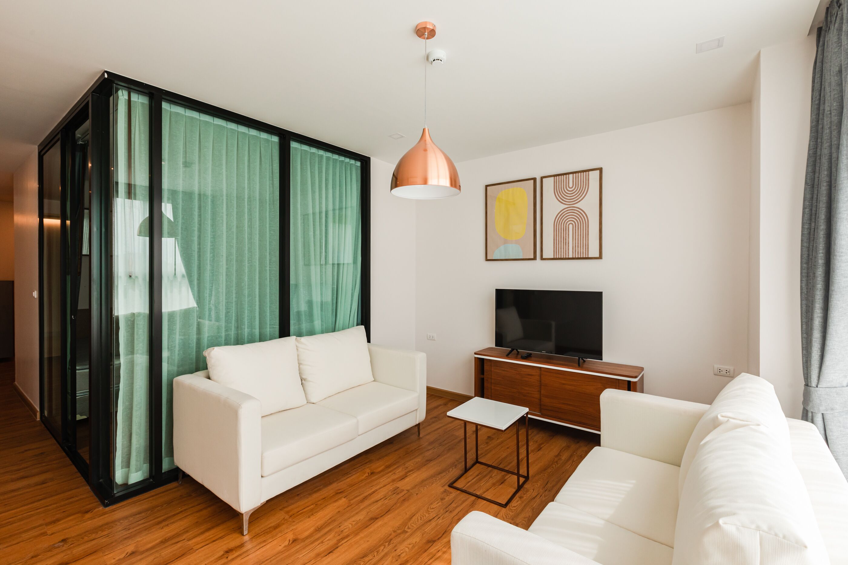 Een moderne woonkamer met een witte bank, een klein bijzettafeltje en een televisie op een houten kast.