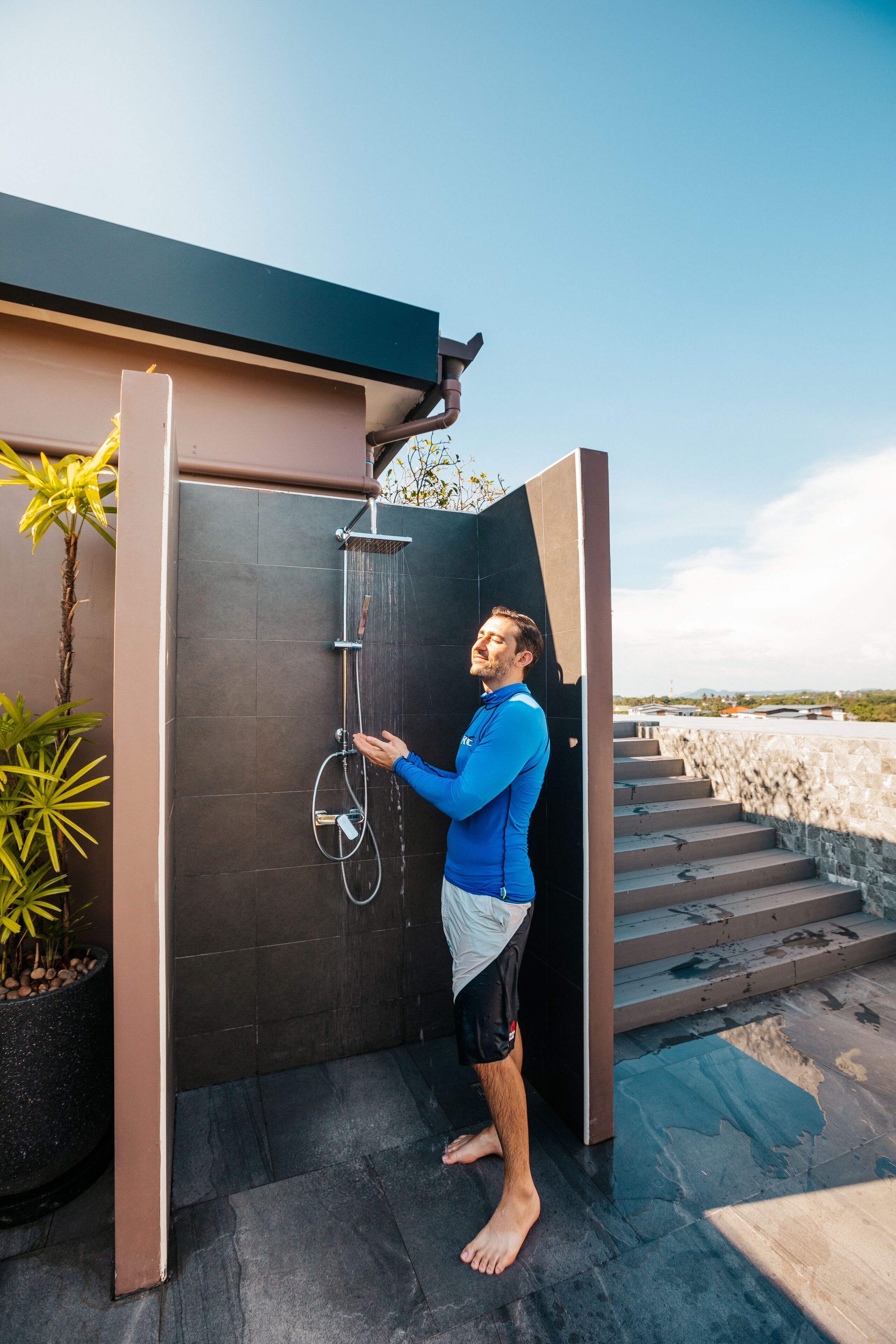 A person standing in a modern outdoor shower area with a view of the landscape.