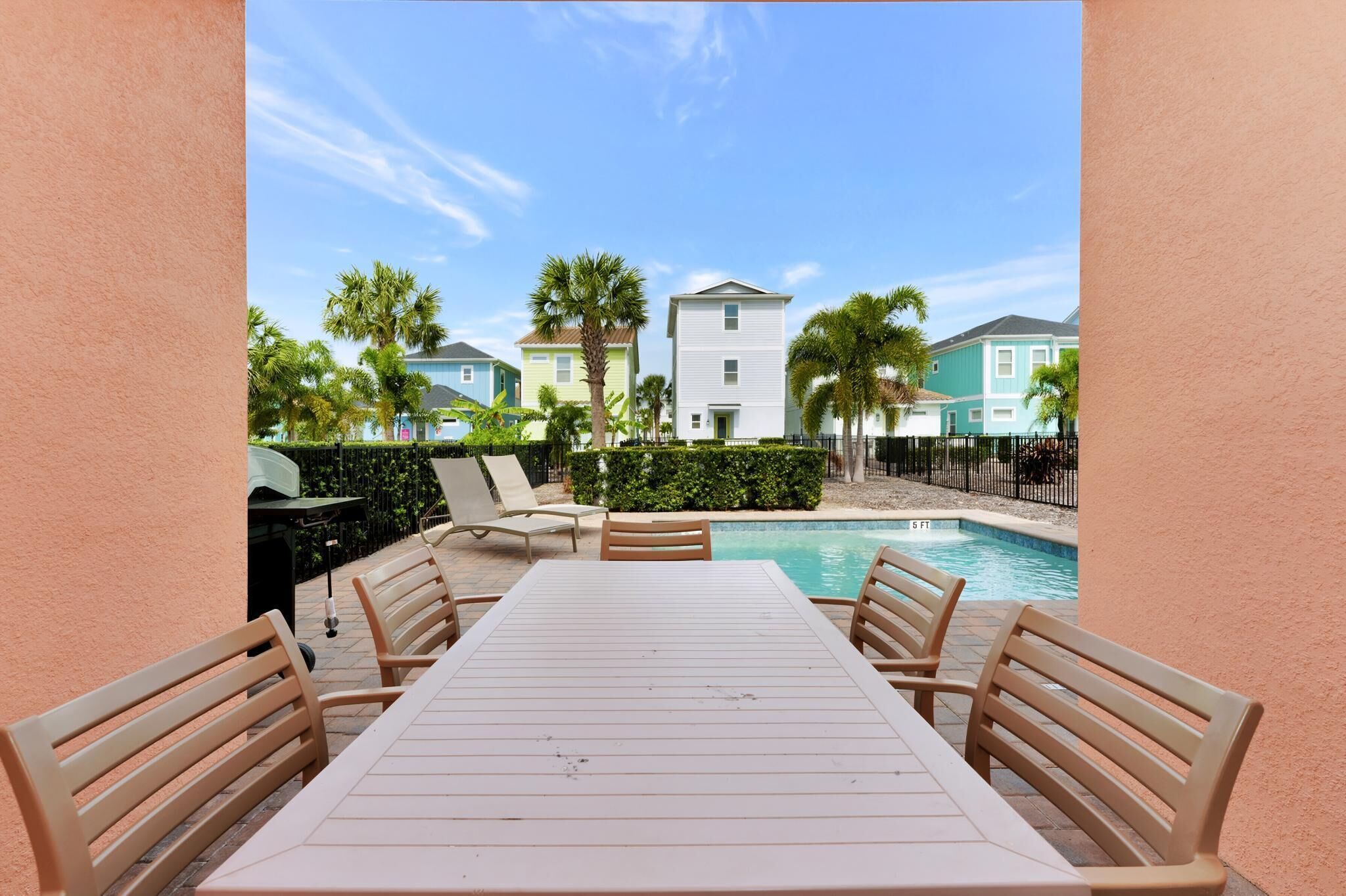 A poolside area with a table and chairs, a pool, and a view of colorful buildings in the background.
