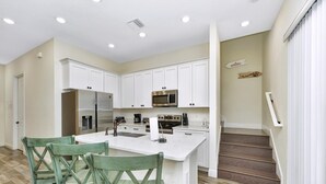 A modern kitchen with white cabinets, stainless steel appliances, and a central island with chairs. - Peachy Dream Cottage near Disney | Pool + Resort & Waterpark Access - 8016KD (Kissimmee)