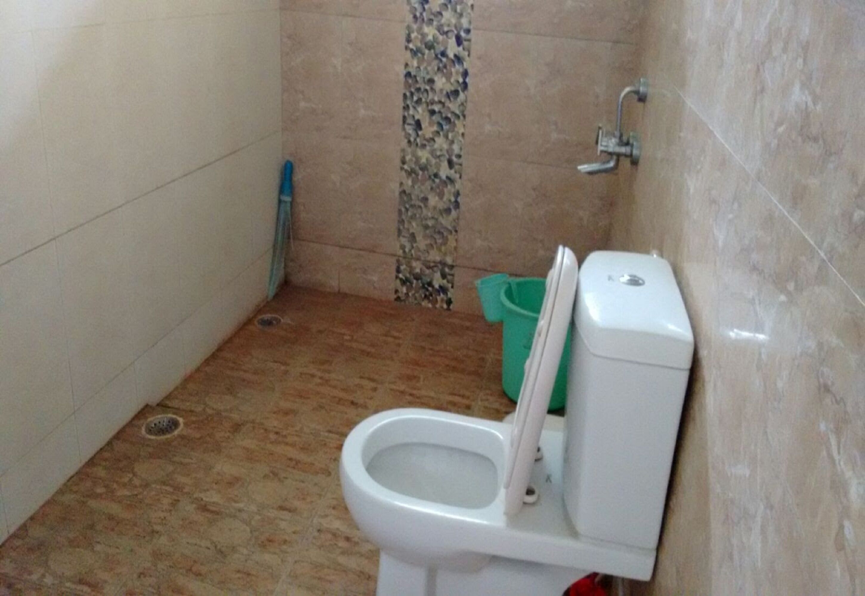 A small bathroom with a toilet, a green trash bin, and a shower area.