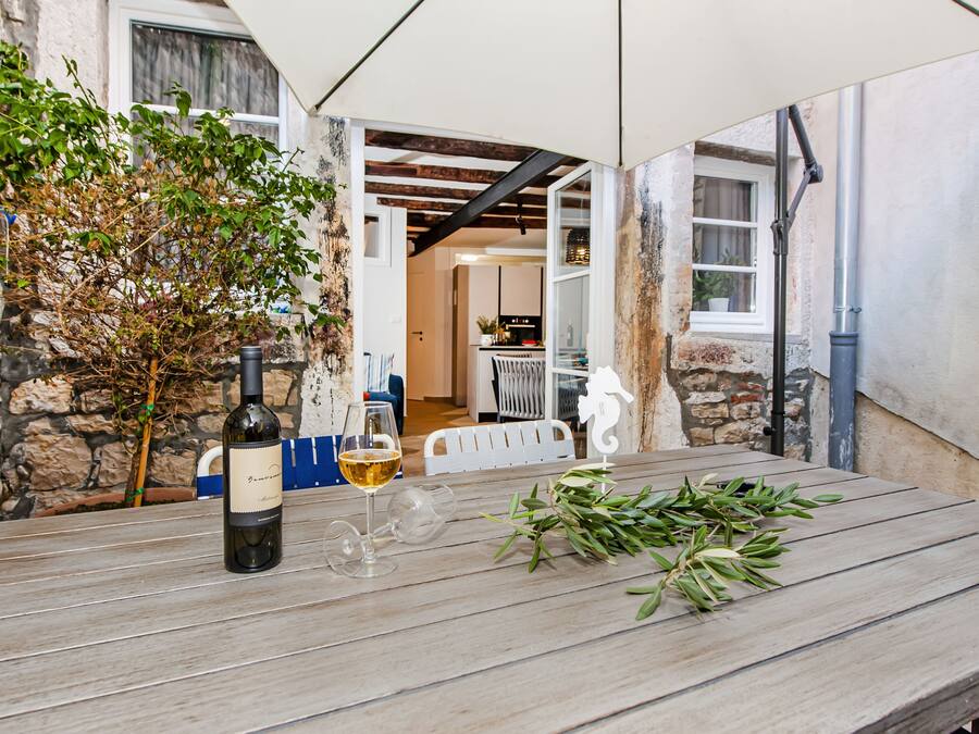 A wooden table with a bottle of wine, a glass, and a branch of greenery.