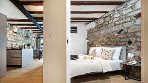 Un dormitorio con pared de piedra, una cama con almohadas, una mesita de noche y una lámpara.