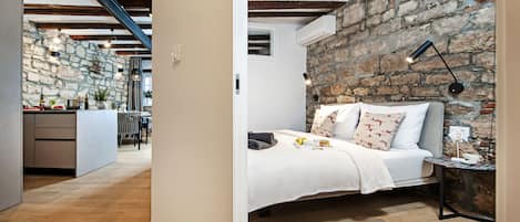 A bedroom with a stone wall, a bed with pillows, a bedside table, and a lamp.