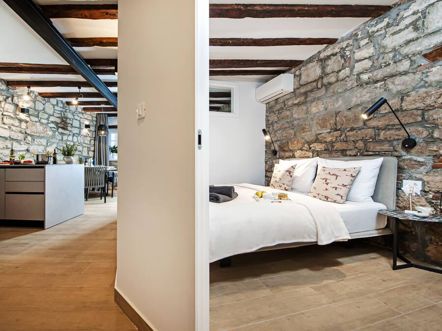 Un dormitorio con pared de piedra, una cama con almohadas, una mesita de noche y una lámpara.