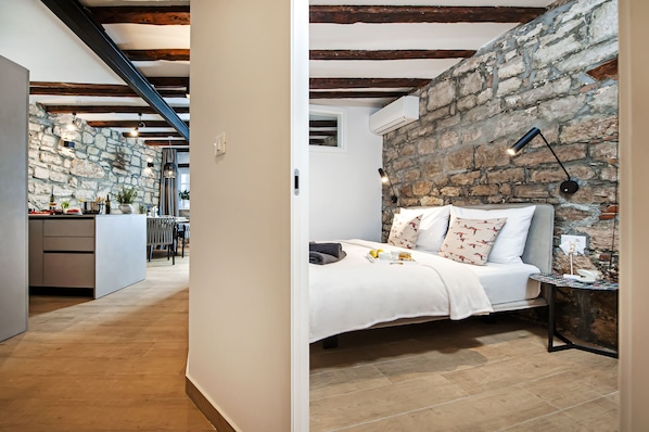 Un dormitorio con pared de piedra, una cama con almohadas, una mesita de noche y una lámpara.
