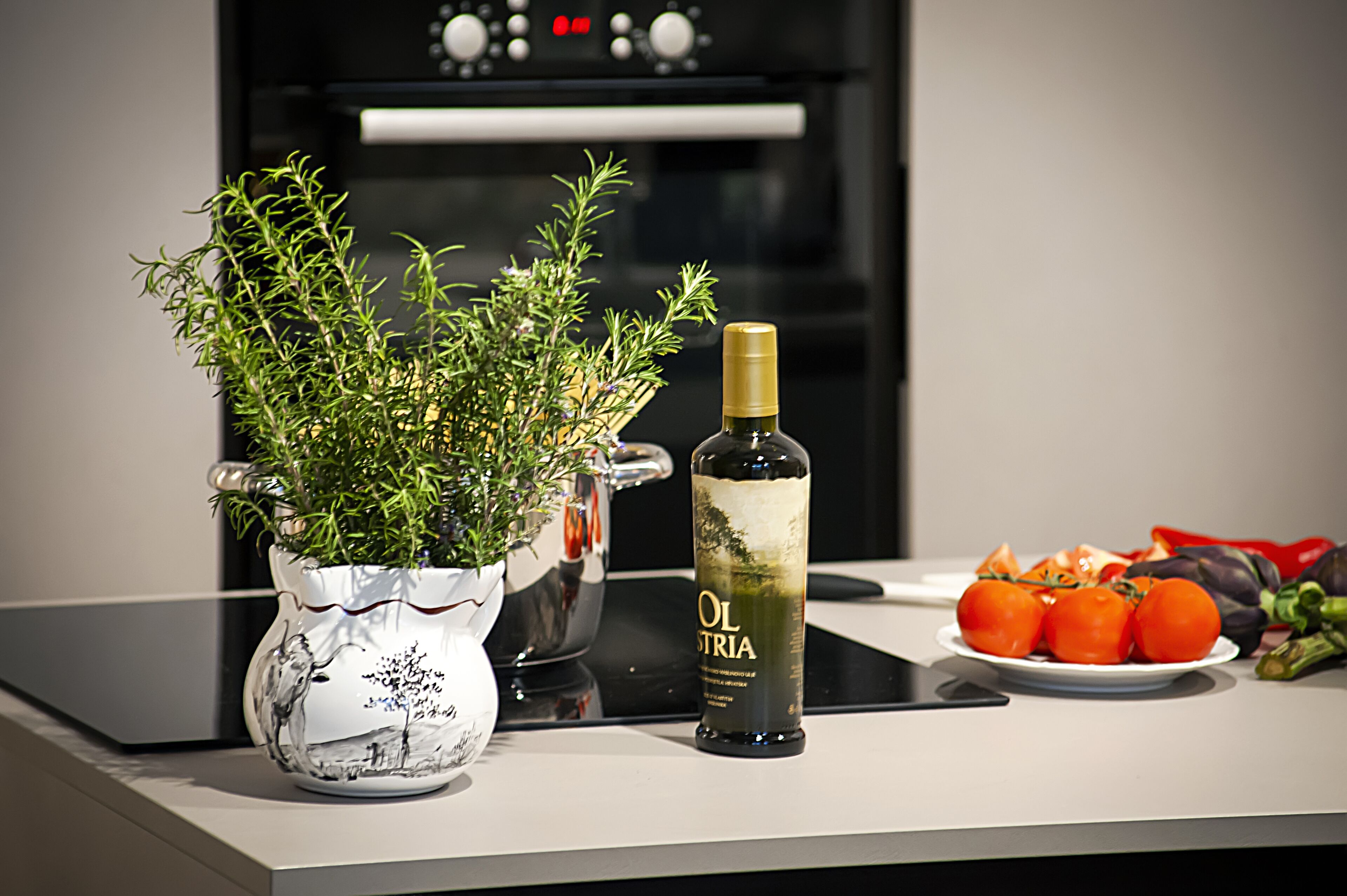 Un piano di lavoro in cucina con una pianta in vaso, una bottiglia d'olio d'oliva e un piatto di pomodori e melanzane.