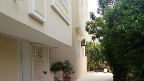 A narrow, tiled courtyard with a gated entrance, potted plants, and a building with a white facade.