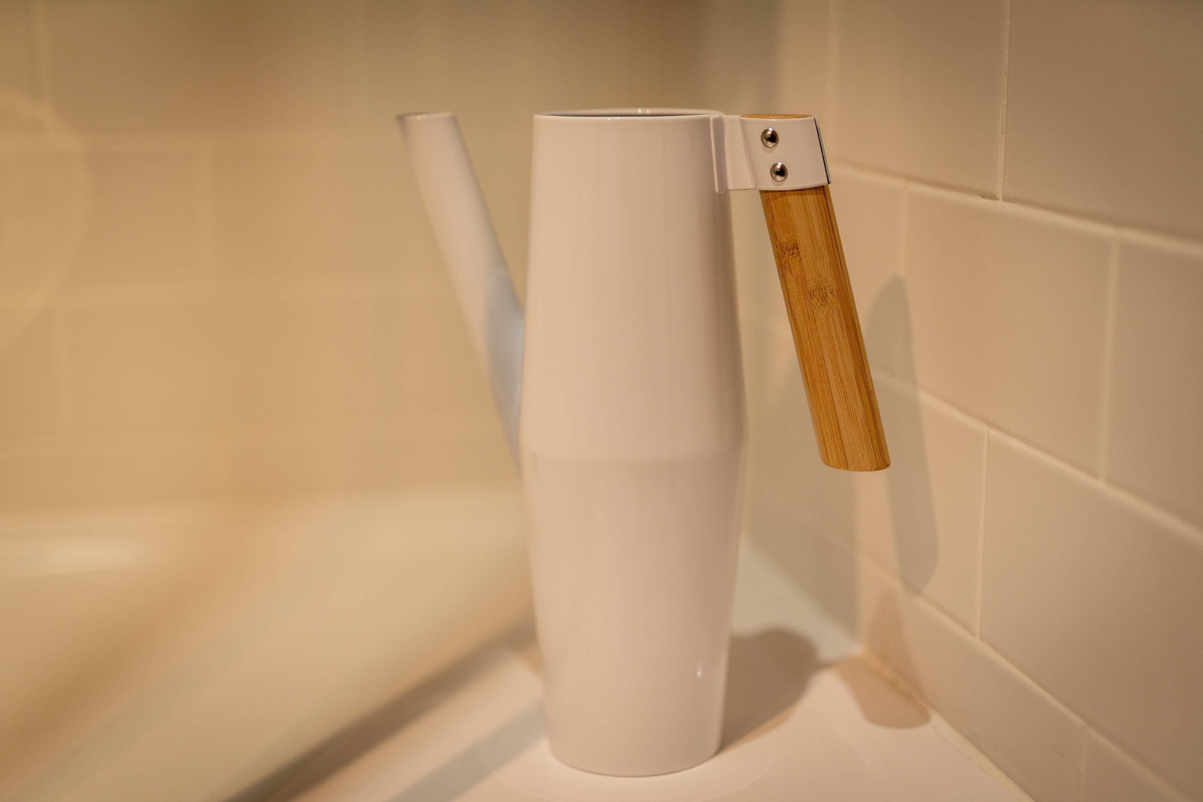 Een witte keramische mok met een houten handvat, bevestigd aan een witte betegelde muur.