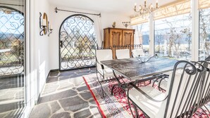 A dining area with a table and chairs, a chandelier, a wooden cabinet, and a view through a window with a metal gate. - Apartment "Im Haus Stöckl" with Mountain View, Garden, Terrace & Wi-Fi (Angerberg)
