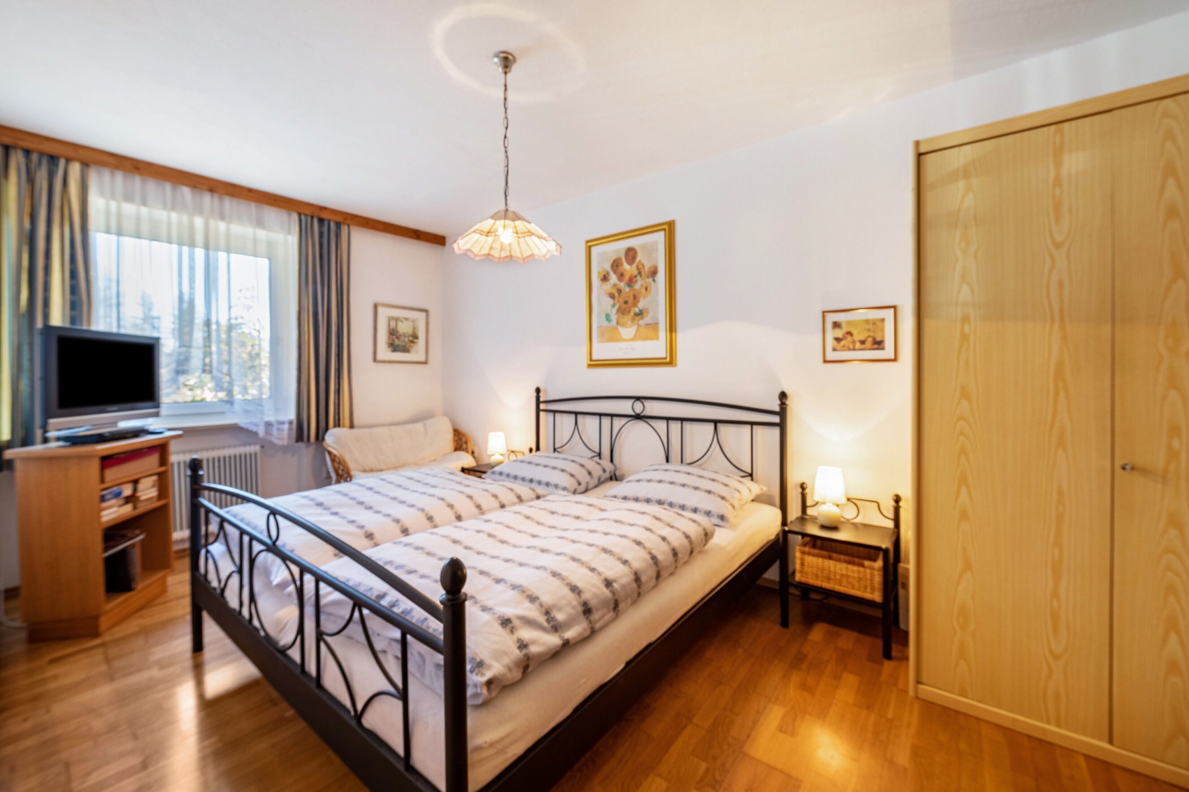 Ein Schlafzimmer mit Bett, Nachttischen, einem Kleiderschrank, einem Schreibtisch mit Computer und einem Fenster mit Vorhängen.