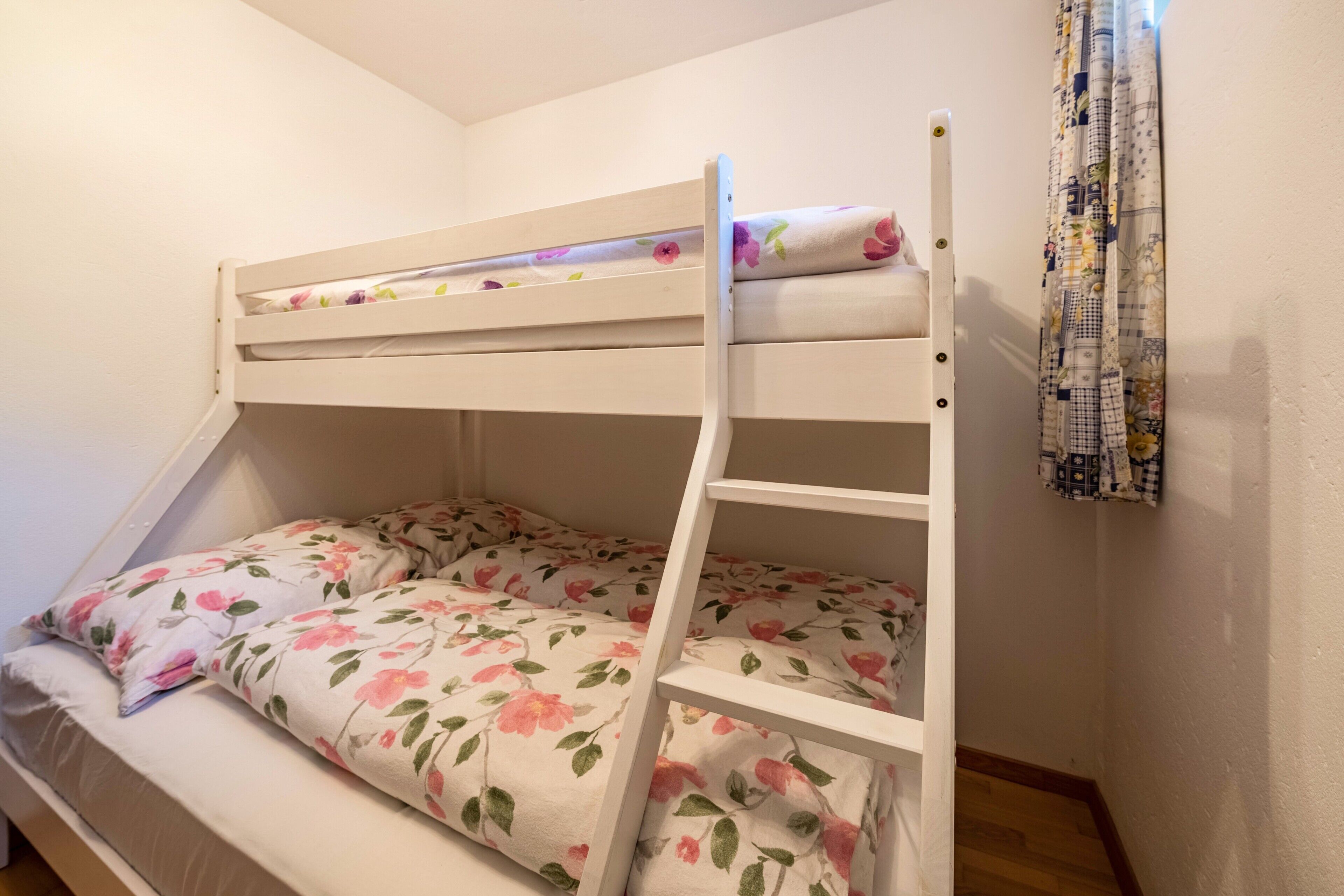 Un lit superposé avec une literie à motifs floraux, une échelle en bois et un rideau à motifs.