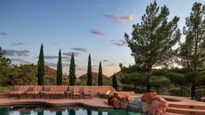 A swimming pool with lounge chairs and a fire feature, surrounded by trees and a hilly landscape. - Hill-top Haven w/ Heated pool & spa, expansive views and more! (Sedona)