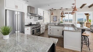 A modern kitchen with white cabinetry, stainless steel appliances, a large island, and pendant lighting. - Hill-top Haven w/ Heated pool & spa, expansive views and more! (Sedona)