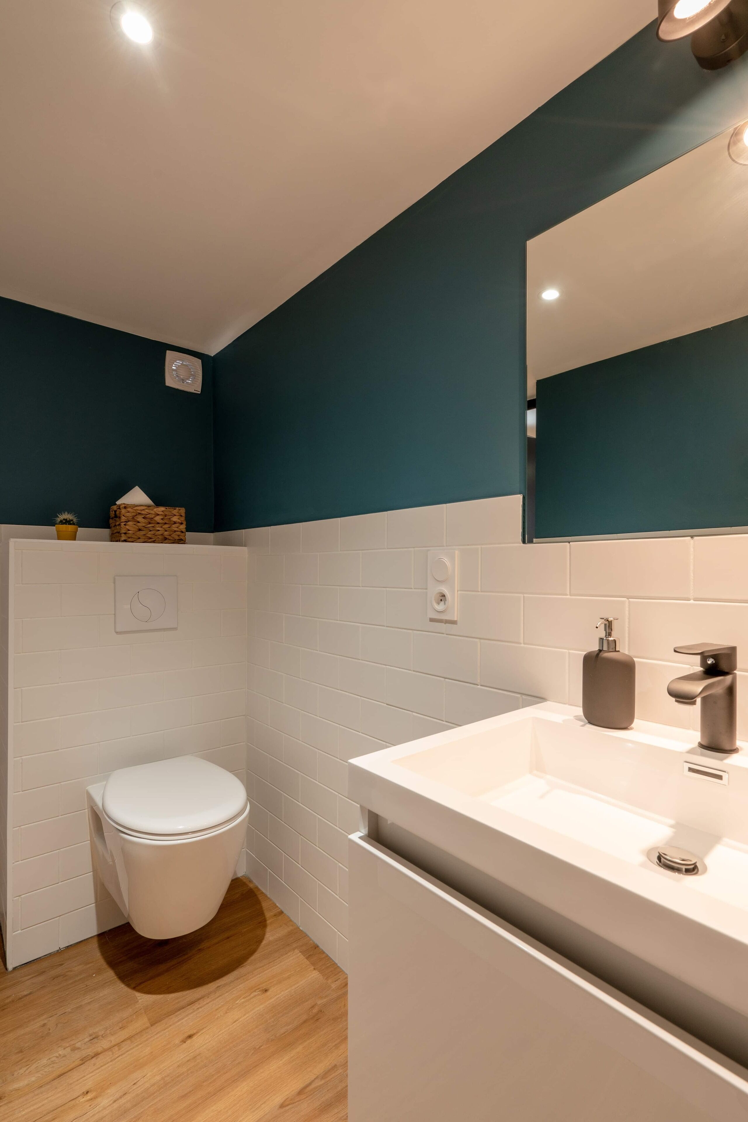 Une salle de bain moderne avec des toilettes blanches, un lavabo avec un miroir et des murs de couleur turquoise.