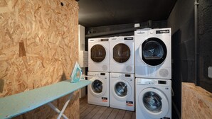 A laundry room with four stacked front-loading washing machines, a blue ironing board, and a wooden wall. - A little bit of greenery and calm in the middle of the city! The 3rd. (La Roche-sur-Yon)