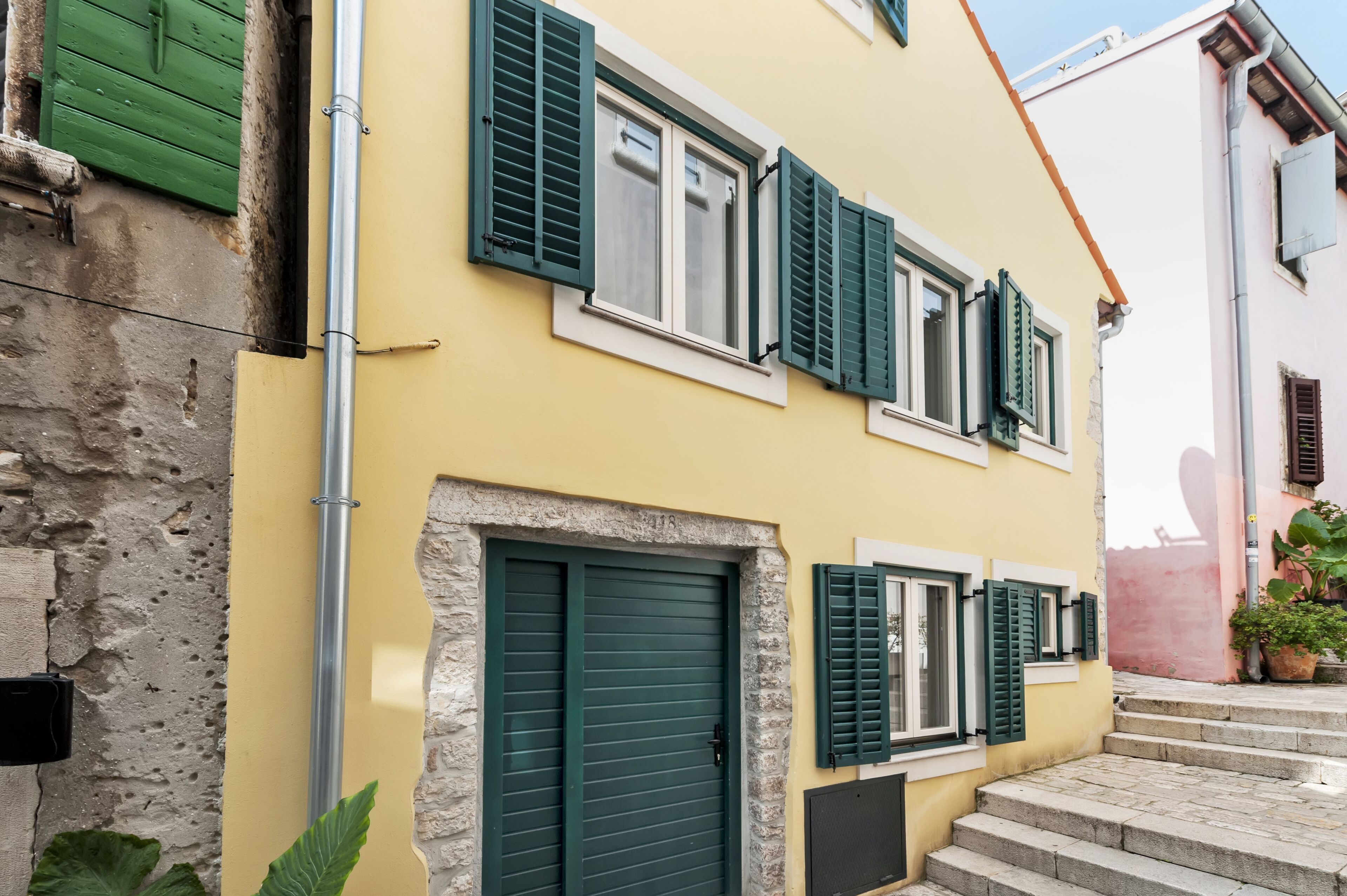 A building with a yellow facade, green shutters, and a stone wall.