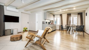 A modern living room with a wooden floor, a flat-screen TV mounted on the wall, a dining area with a table and chairs, and a kitchen in the background. - Yellow House Rovinj (Rovinj)