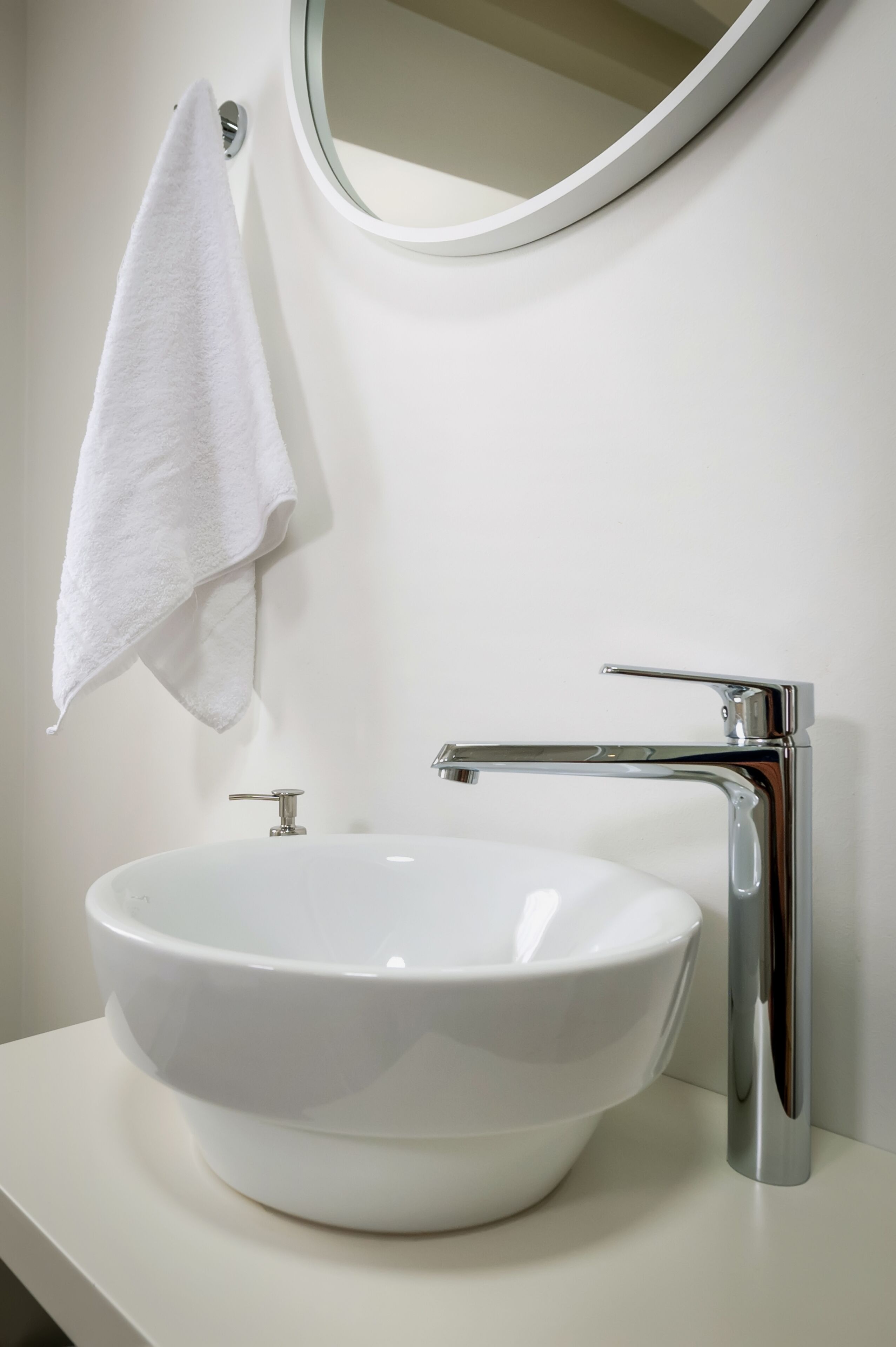 A white bathroom sink with a chrome faucet and a round mirror above it.