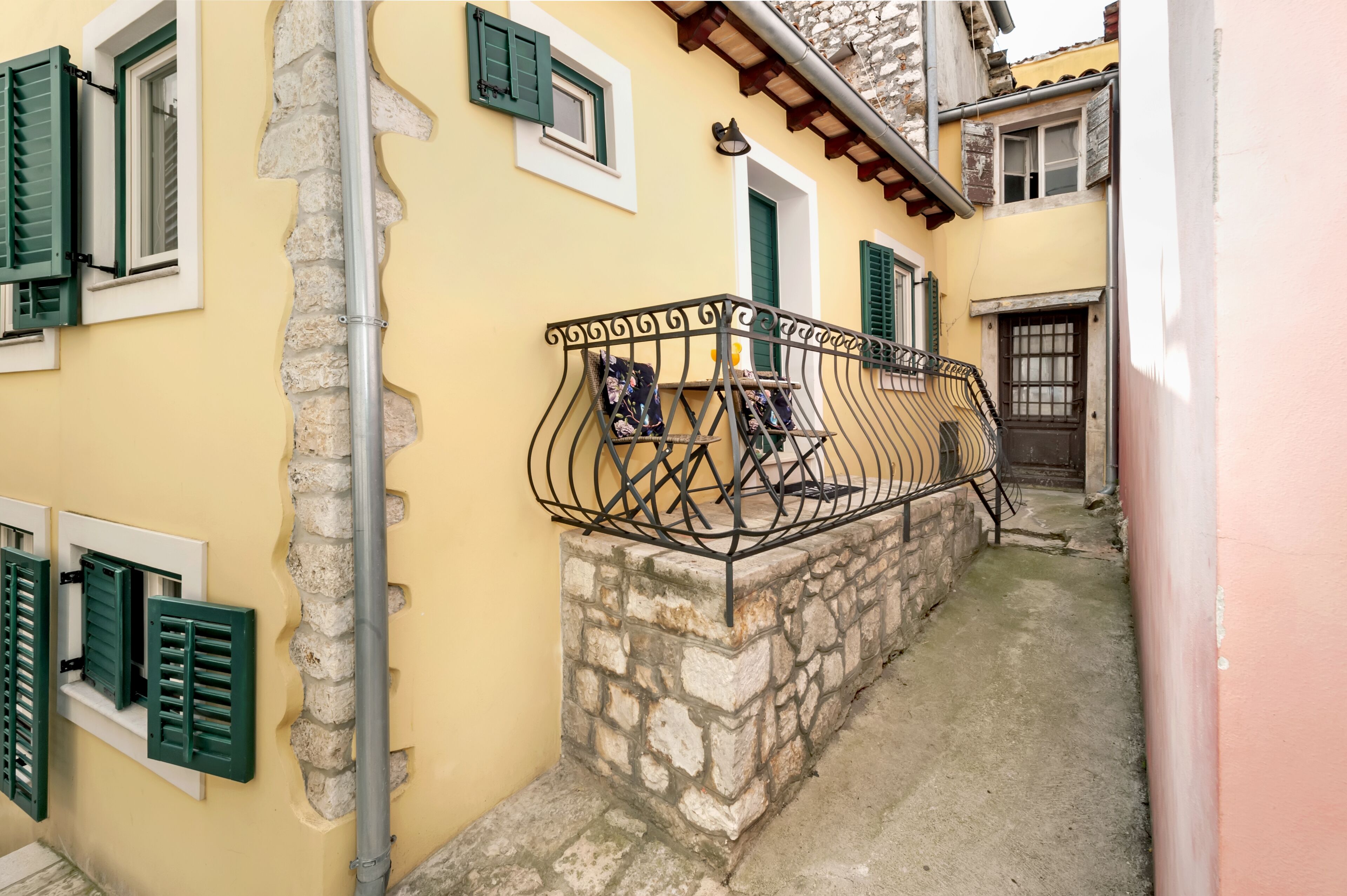 A narrow alleyway with a stone wall, a metal railing, and a door with a window.