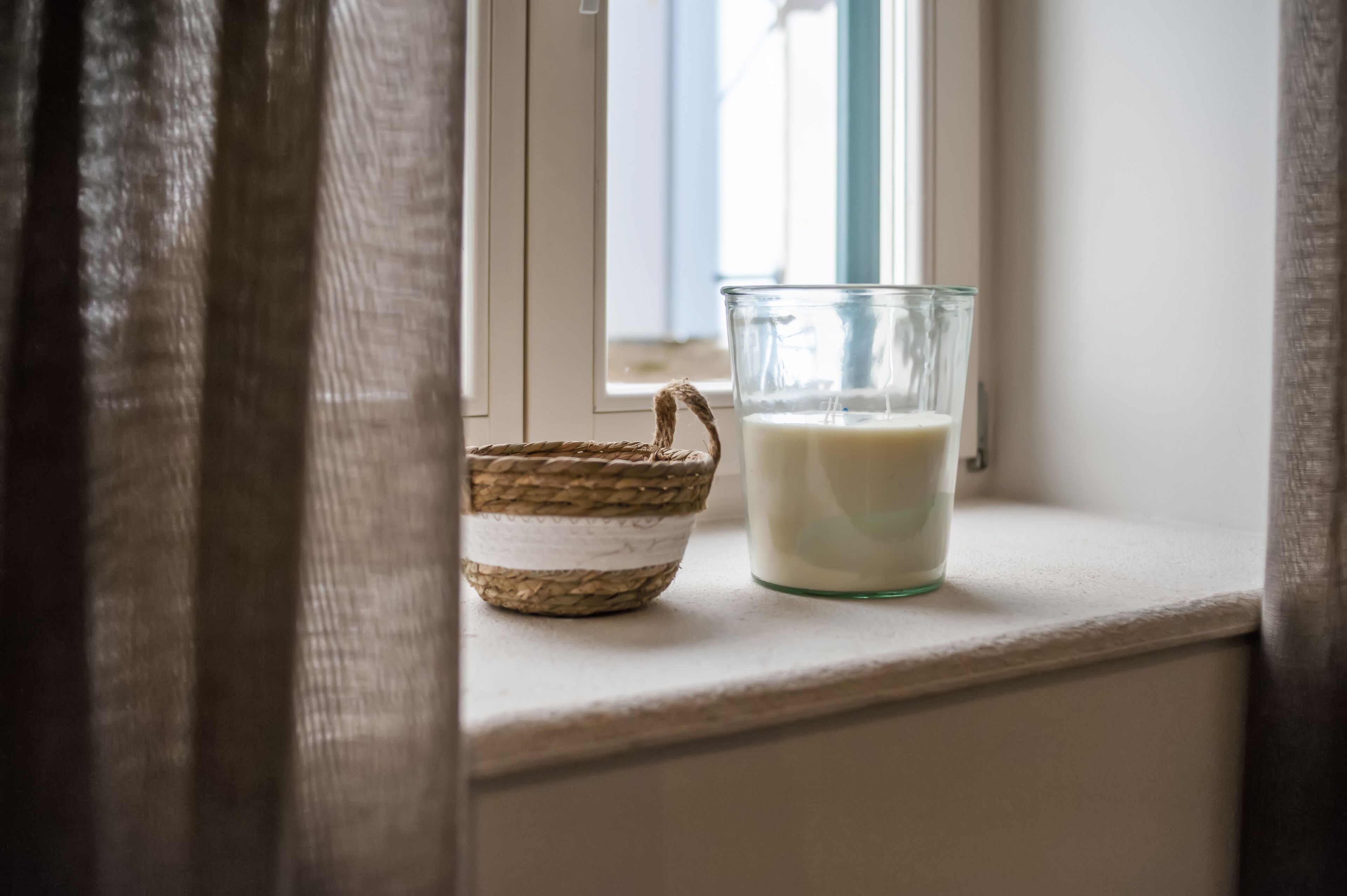 A glass of milk on a windowsill next to a woven basket.