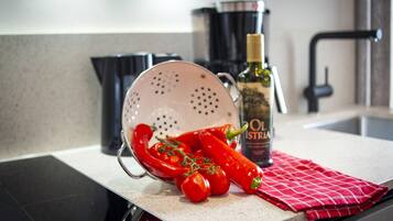 A kitchen counter with a colander, red chili peppers, a bottle of olive oil, and a red checkered cloth.
