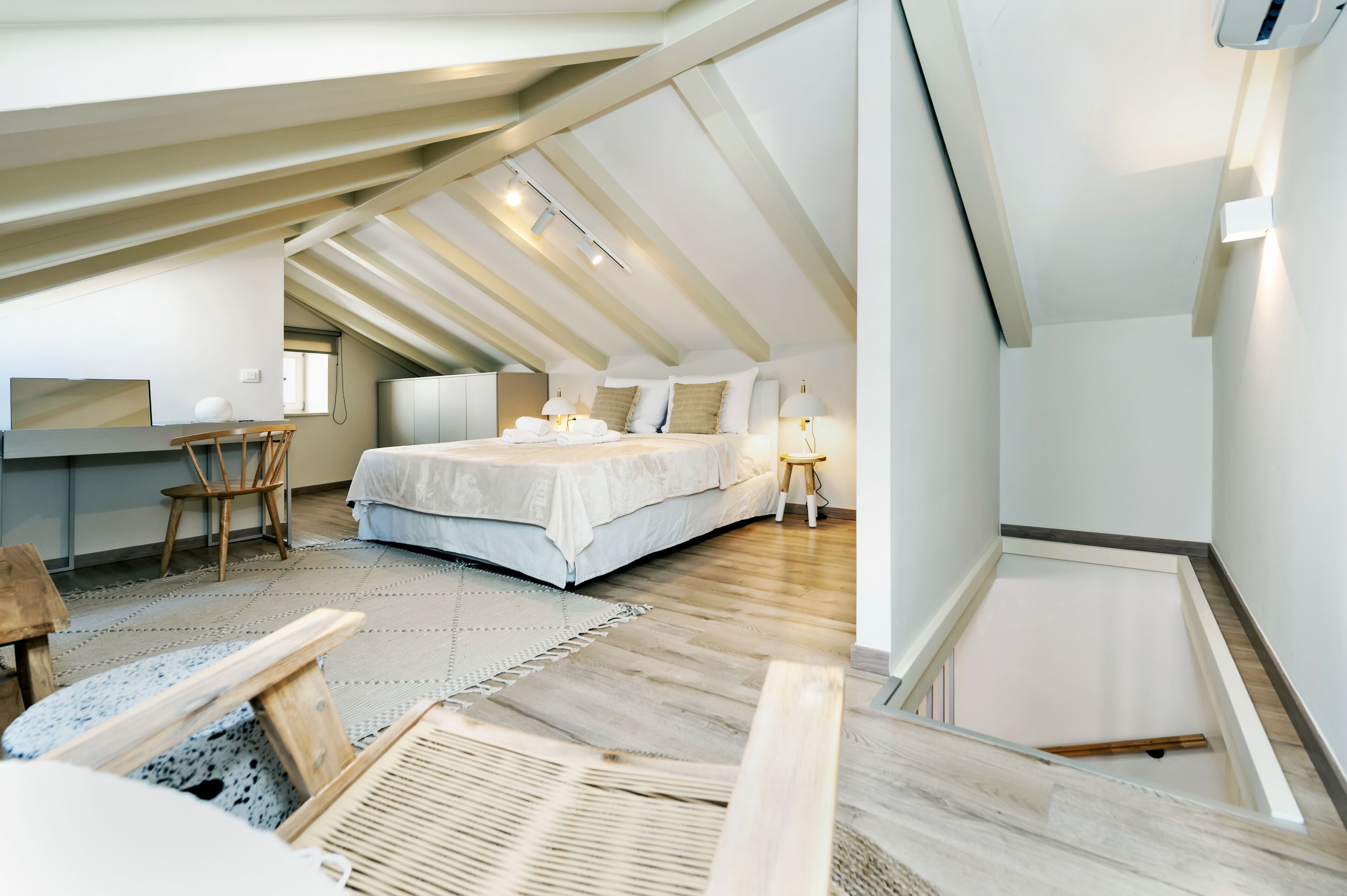 Un dormitorio tipo loft moderno con techo inclinado, una cama grande, un escritorio y una silla.