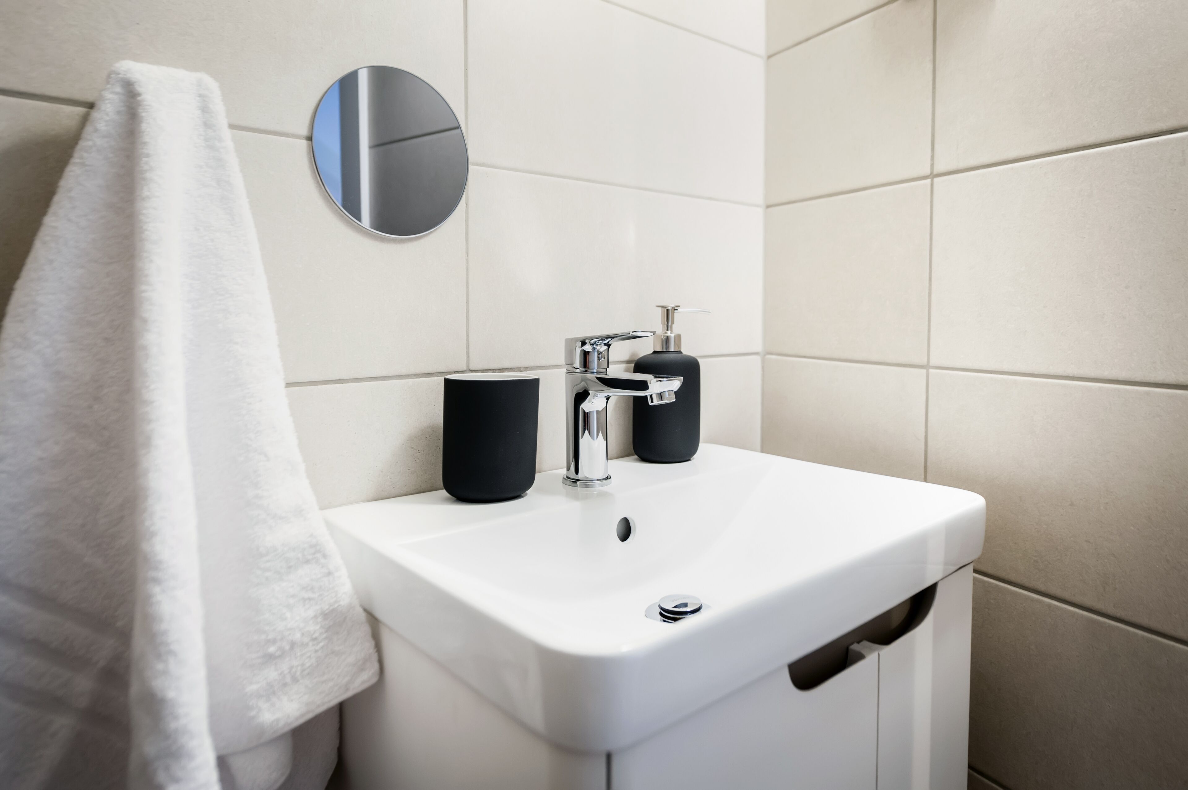 A modern bathroom with a white sink, a round mirror, and a towel hanging on the wall.