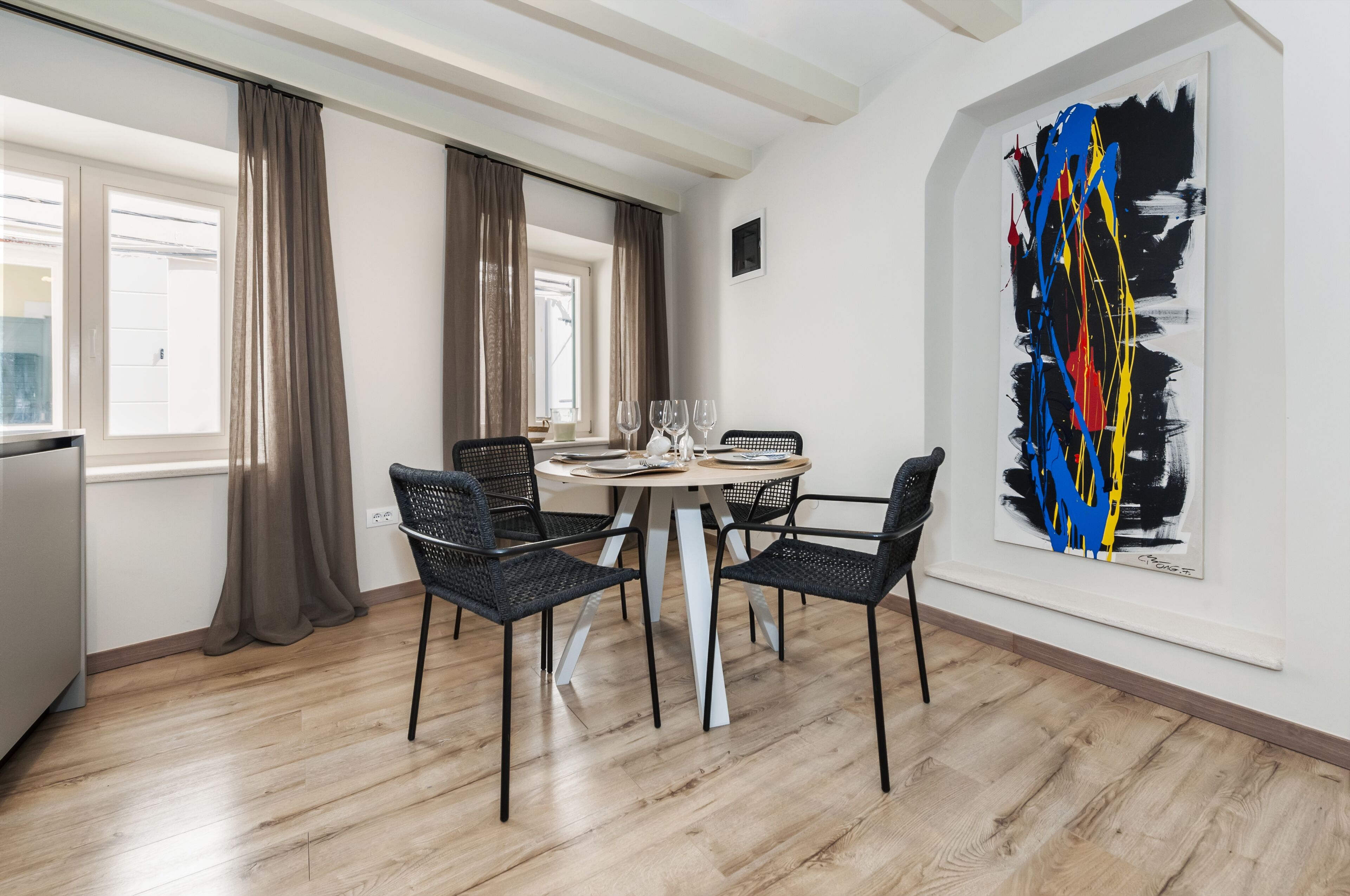 Un'area pranzo con un tavolo rotondo, quattro sedie e un grande quadro astratto appeso al muro.