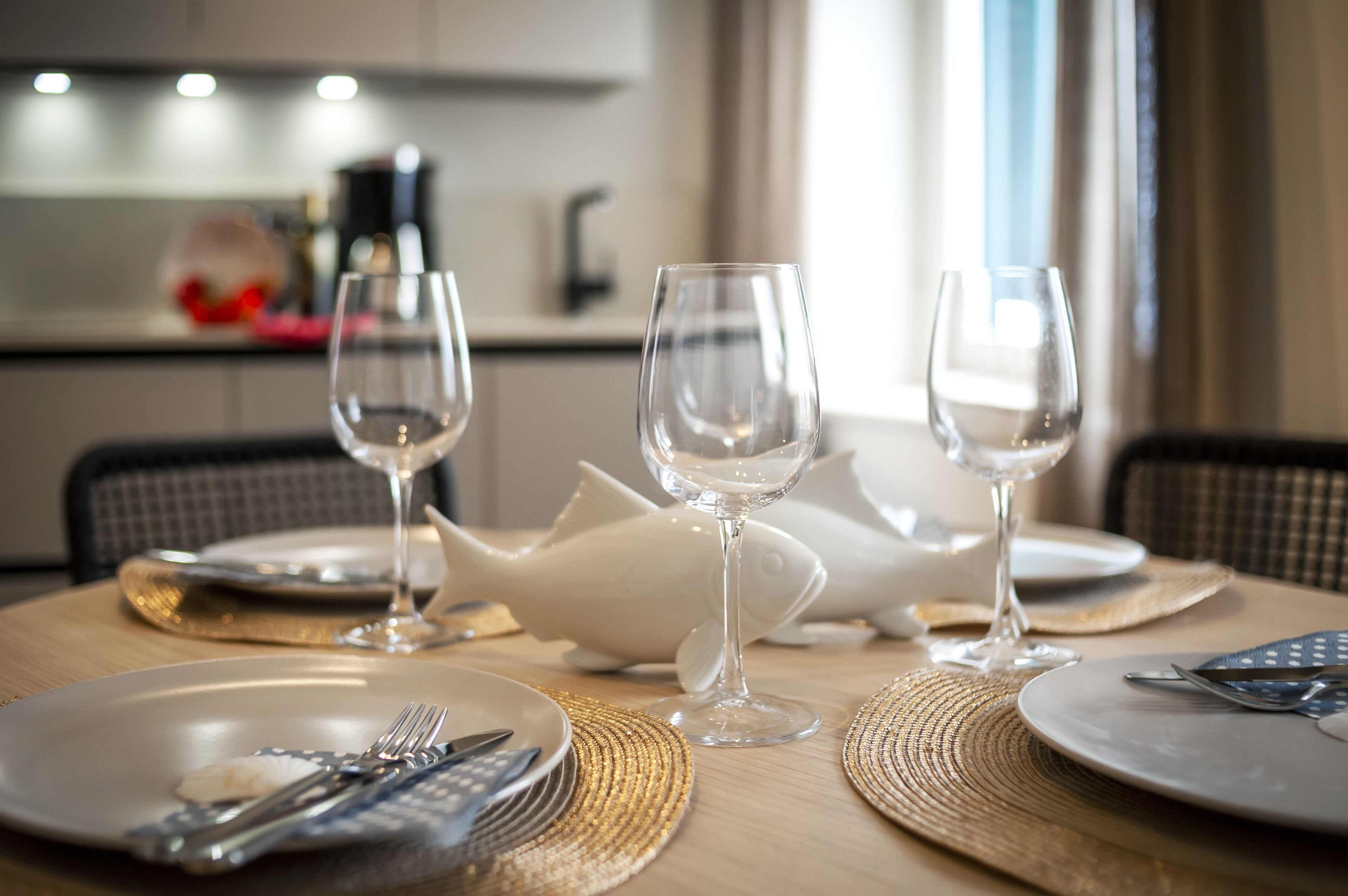 Una mesa de comedor dispuesta con tres copas de vino, un centro de mesa con forma de pez y platos con cubiertos.