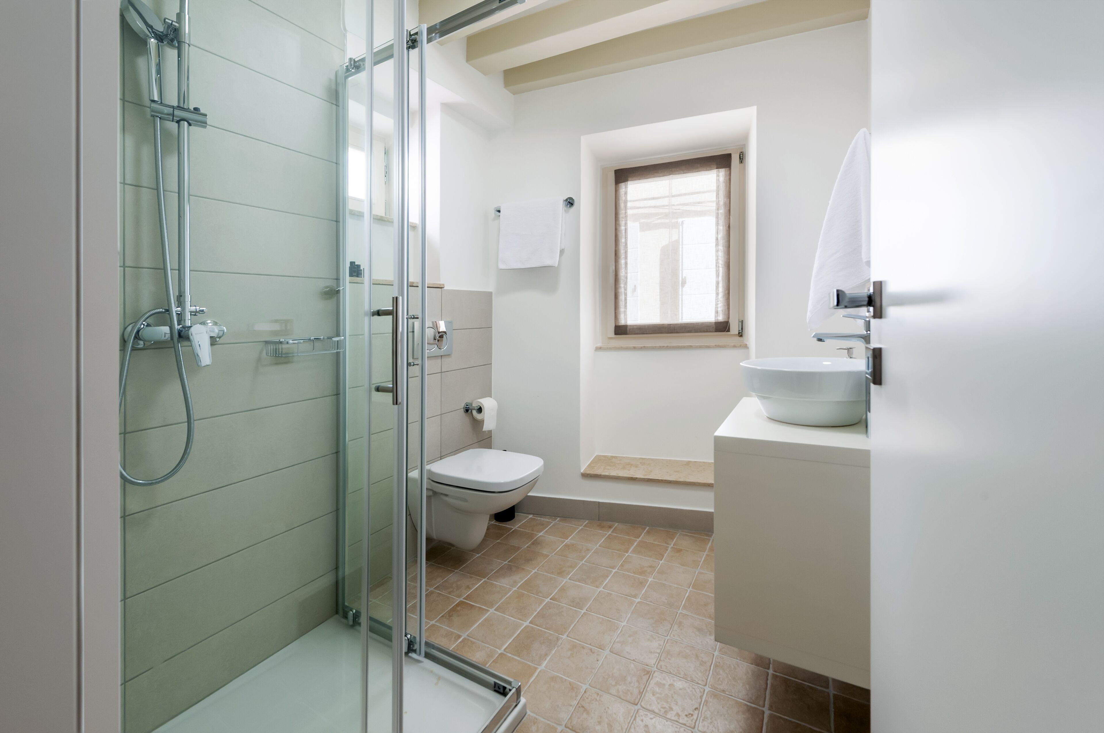 Un baño con ducha de vidrio, inodoro, lavamanos y ventana.