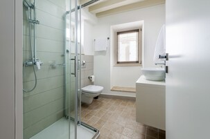 A bathroom with a glass-enclosed shower, a toilet, a sink, and a window.