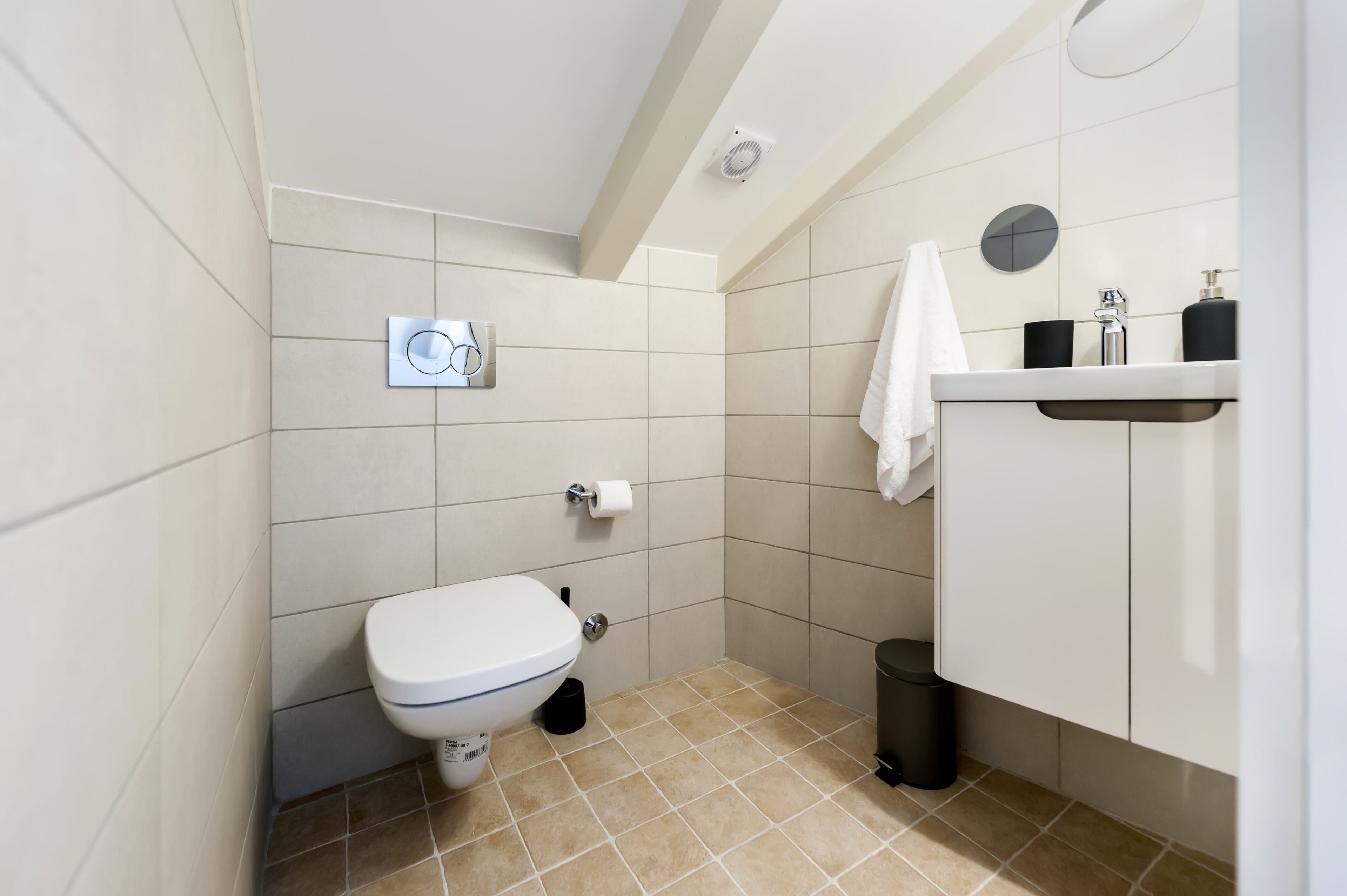 A small, modern bathroom with a toilet, sink, and a towel hanging on the wall.