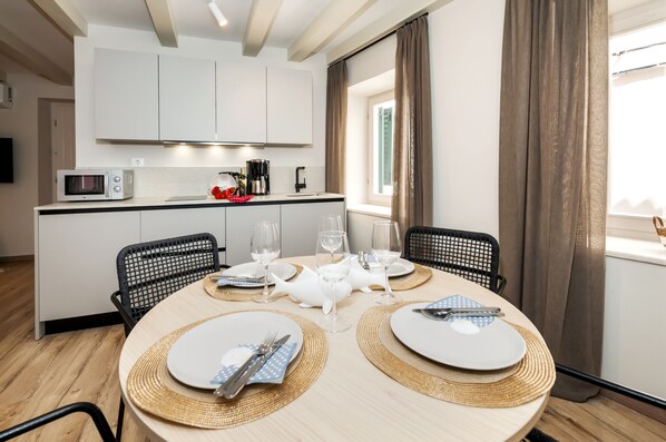 Une cuisine moderne avec des meubles blancs, un four à micro-ondes et une machine à café. On y trouve une table à manger, mise avec des assiettes, des couverts et des verres.