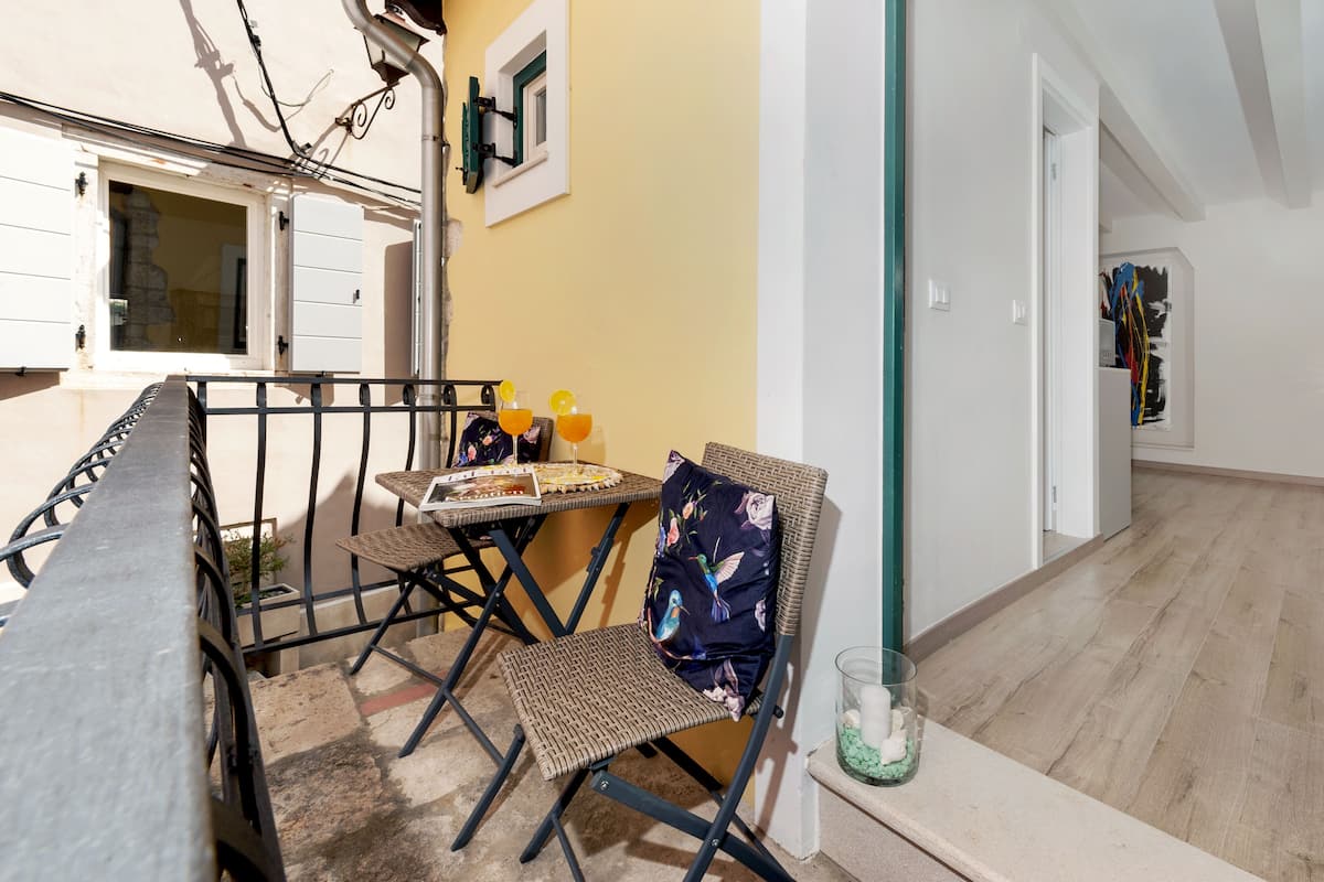 A dining area with a table and chairs, a small table with drinks, and a chair with a cushion.