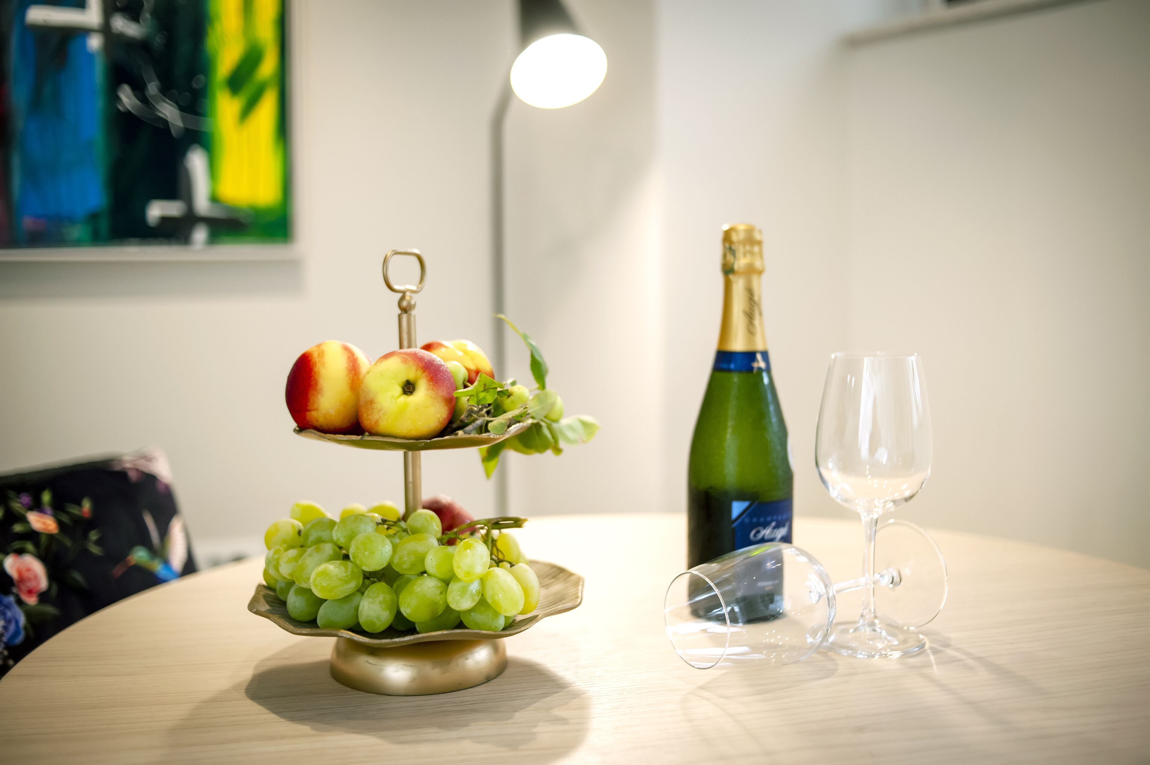 Una mesa con una presentación de frutas, una botella de champán y una copa de vino.