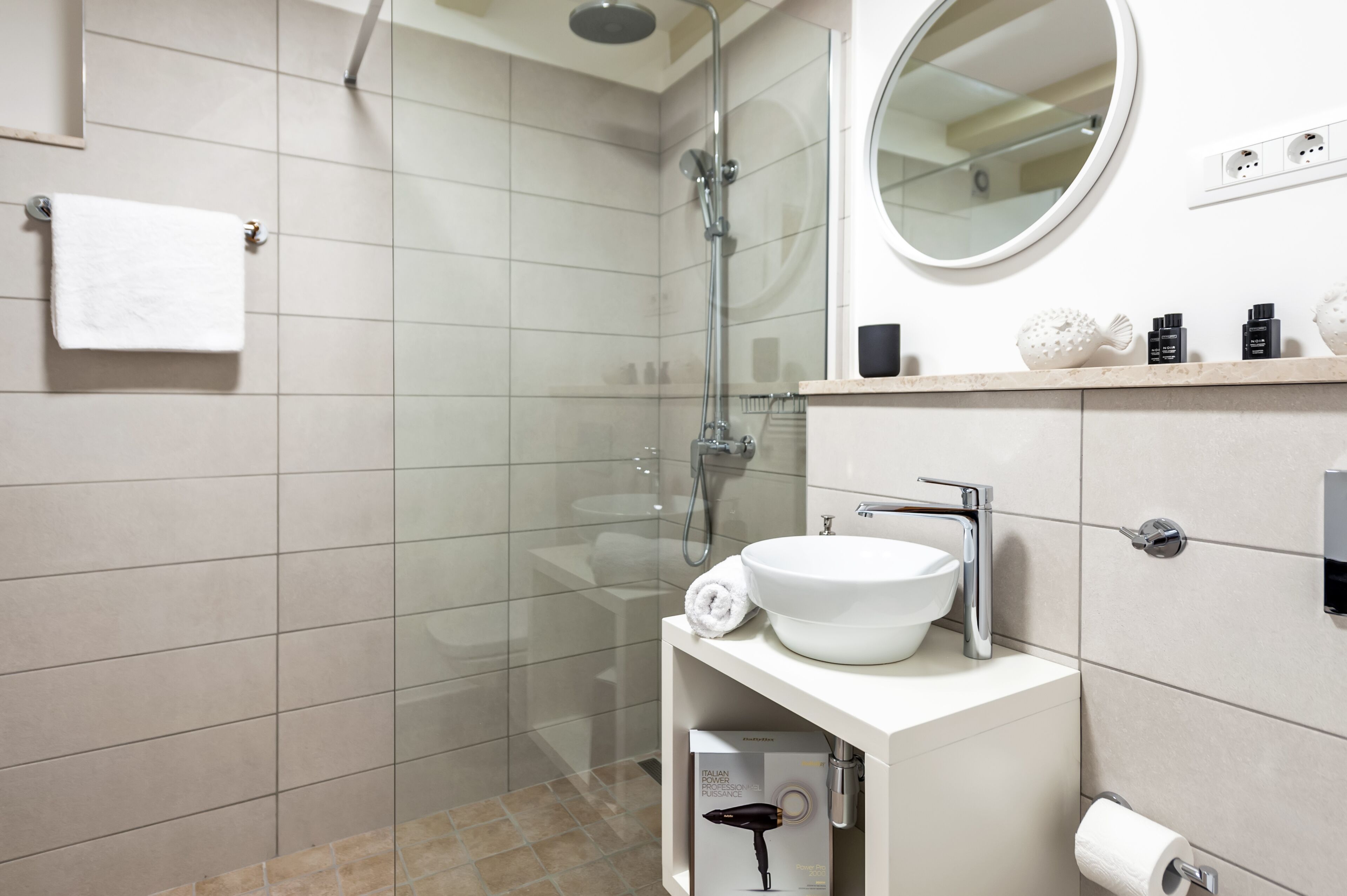 A modern bathroom with a glass-enclosed shower, a white sink, and a round mirror.