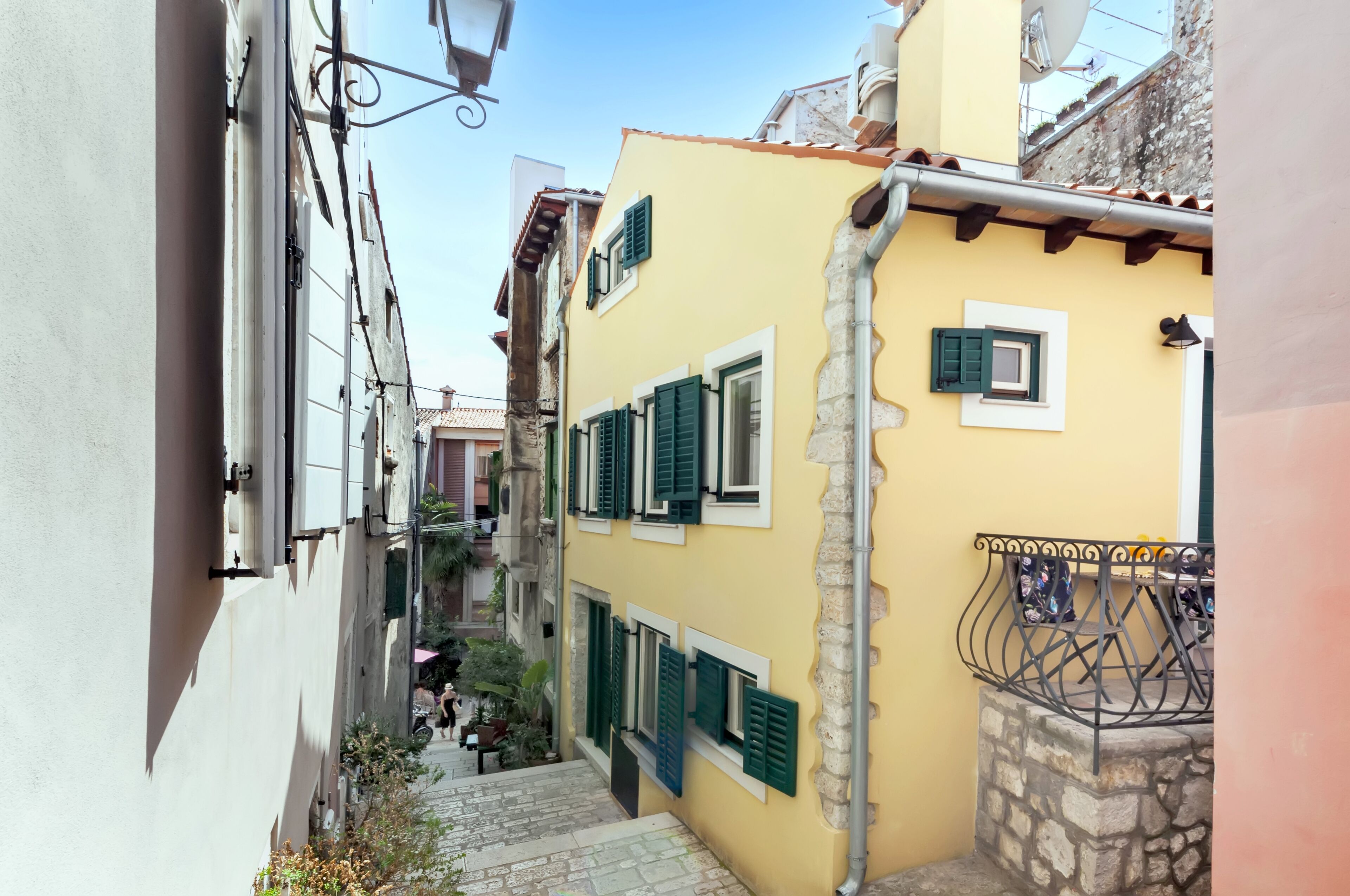 Une rue étroite avec un bâtiment jaune, des marches en pierre et une rambarde en métal.