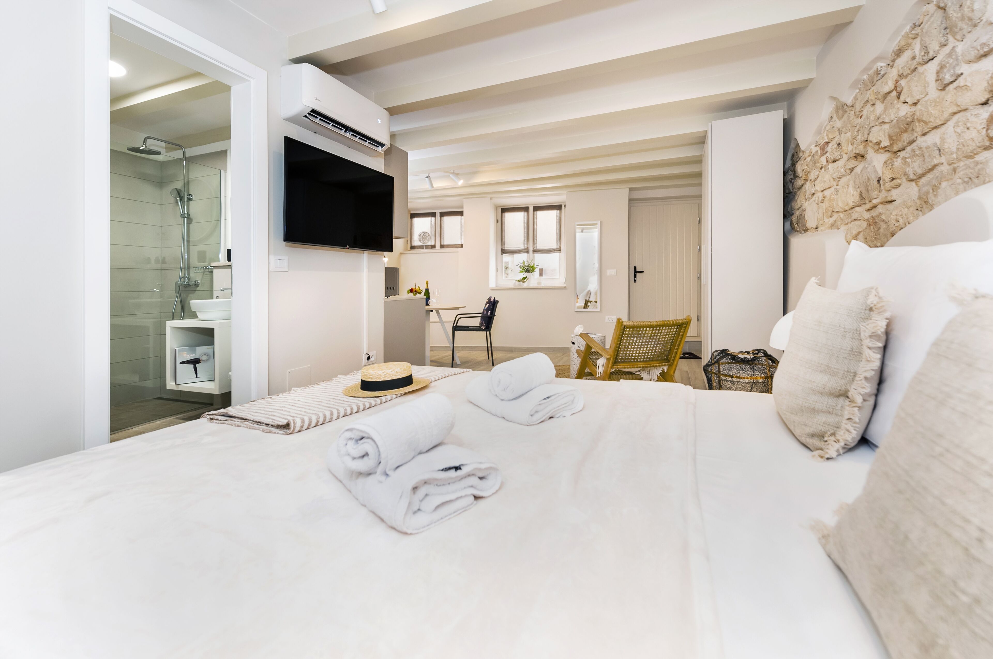 A modern bedroom with a large bed, a TV mounted on the wall, and a stone accent wall.