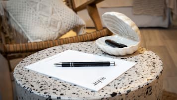 Ein runder Tisch mit Notizbuch und Stift, einer Keramiktasse und einem Korbstuhl im Hintergrund.