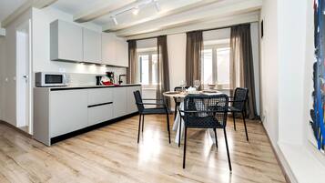 A modern kitchen with white cabinets, a microwave, and a coffee machine. There is a dining area with a round table and four chairs.