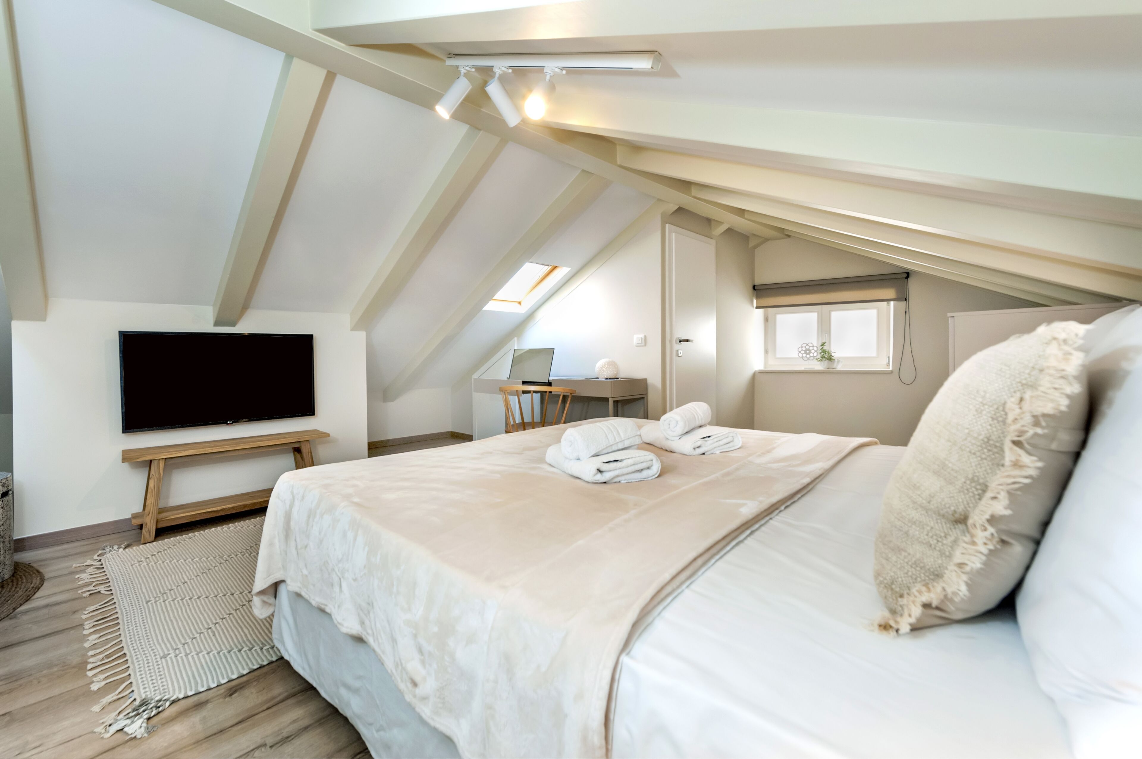 A bedroom with a large bed, a flat-screen TV, a desk, and a window.