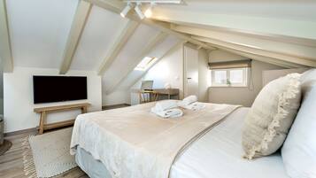 A bedroom with a large bed, a flat-screen TV, a desk, and a window.