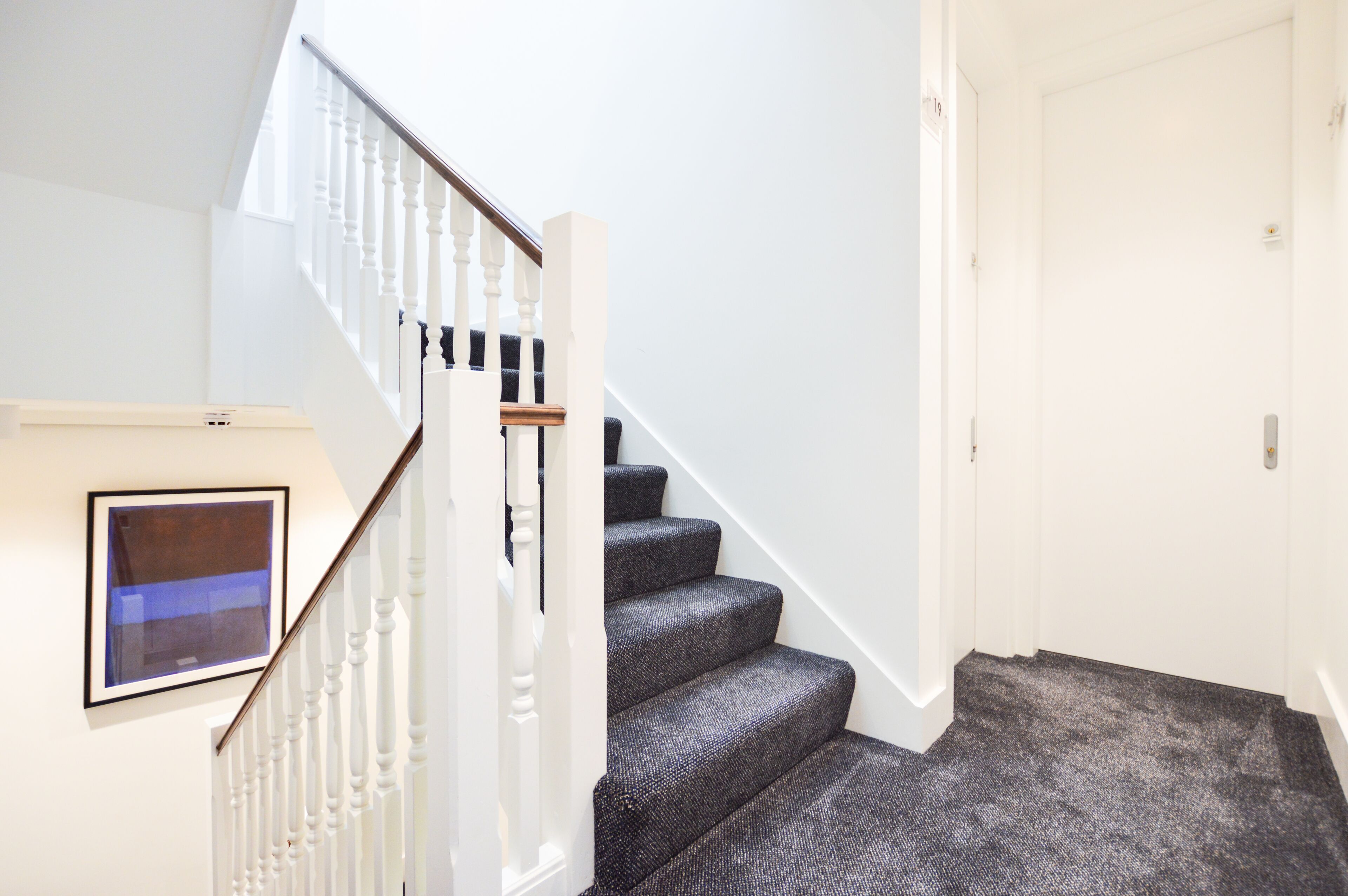 A staircase with white balusters and dark carpeted steps leading to a white door.